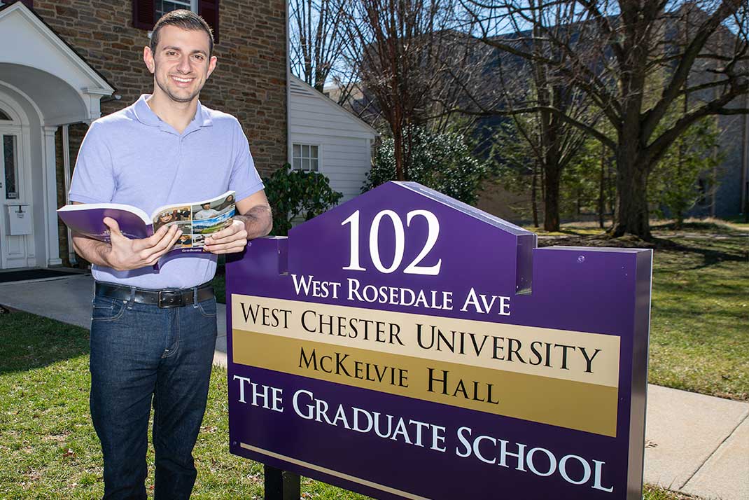 
						Student infront of graduate school sign
					