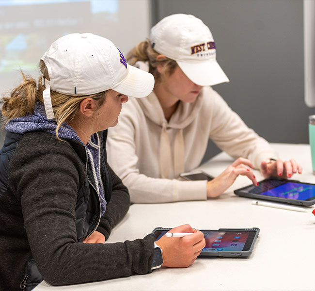 two women in WCU hats are using their Ipads