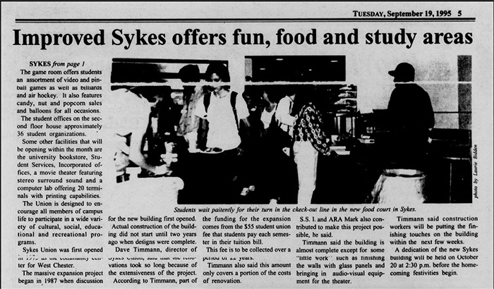 A newspaper article published on Tuesday, September 19, 1995. The headline reads “Improved Sykes offers fun, food and study areas.” A photograph beneath the headline shows students waiting in a line at the food court inside Sykes Union. The article text describes renovations and new features in the building, including food services, recreational areas, and study spaces. A caption under the photograph states that students are waiting patiently for their turn in the check-out line in the new food court in Sykes.