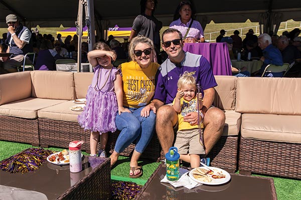 A couple wearing WCU gear is featured smiling and sitting on an outdoor couch with their two young children, who are also wearing WCU colors