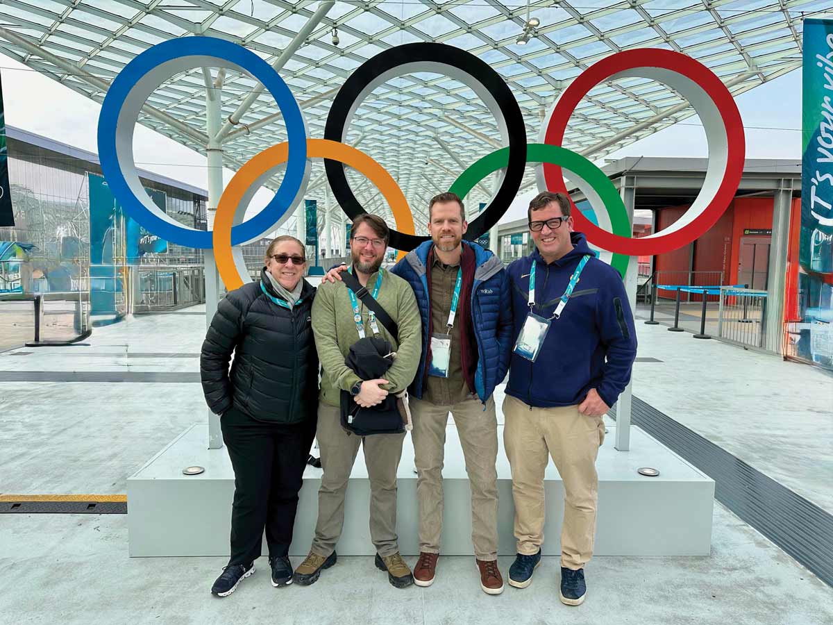 4 people stand and pose for an image in front of the olympic rings
