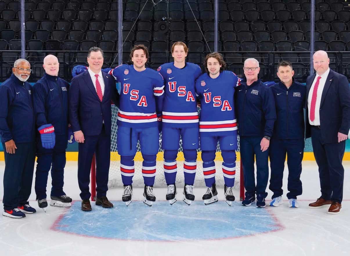 A group of people, 3 usa hockey players in the middle, and various men in suits and athletic gear posing for a picture on the ice rink