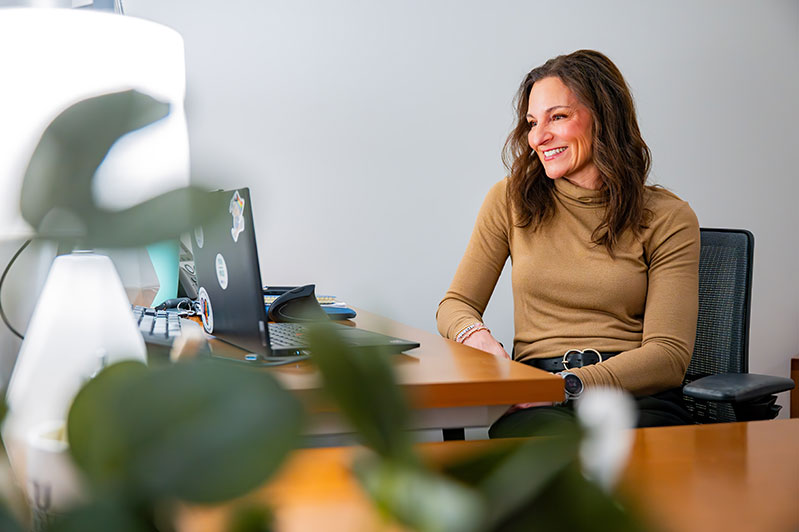 A person sits at a desk, smiling while looking at a computer screen in a bright, modern office space.