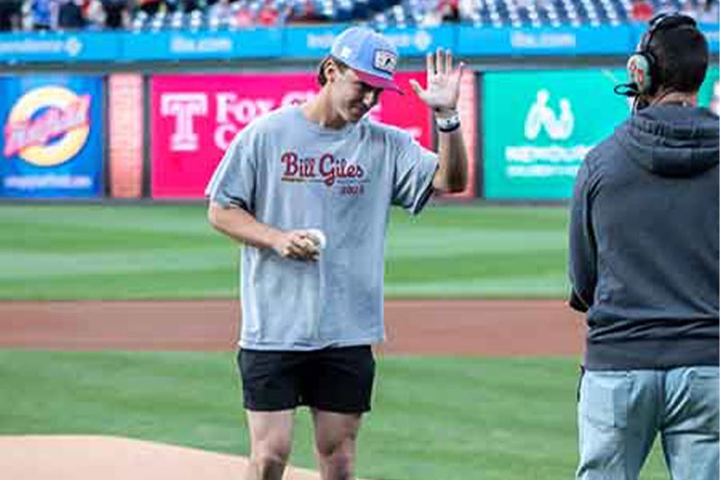 Thumbnail: Jake Welsch is talking to the cameraman and waving before throwing the first pitch