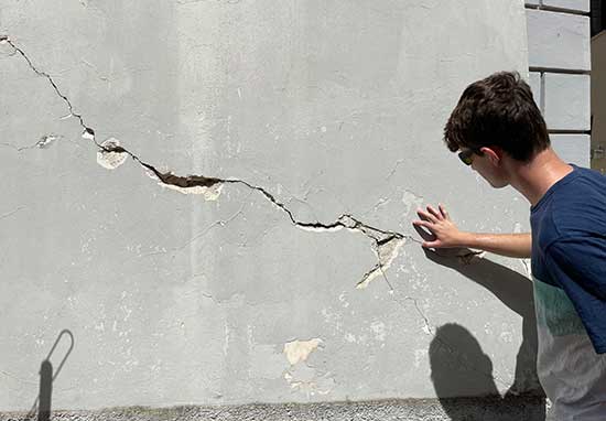 student posing in front of cracked building
